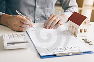 New home buyer signing contract on desk in office room.