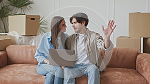 New home decoration. Young happy married man and woman choosing furniture online, sitting with laptop on sofa