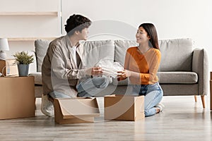 New home. Happy young Asian couple unpacking their belongings from cardboard boxes on moving day