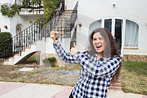 New home, house, property and tenant - Young funny woman holding key in front of her new home after buying real estate