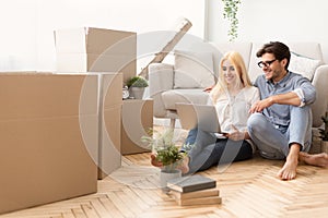 New Home. Husband And Wife Using Laptop Sitting On Floor