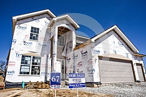 New home partially finished, under construction in residential housing subdivision with for sale sign in yard