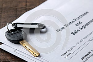 New home purchase and sale agreement. Key with keyring and blank on a brown wooden table. concept of buying a home