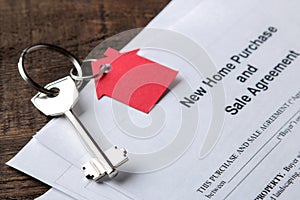 New home purchase and sale agreement. Key with keyring and blank on a brown wooden table. concept of buying a home