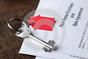 New home purchase and sale agreement. Key with keyring and blank on a brown wooden table. concept of buying a home