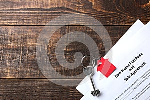 New home purchase and sale agreement. Key with keyring and blank on a brown wooden table. concept of buying a home. top view