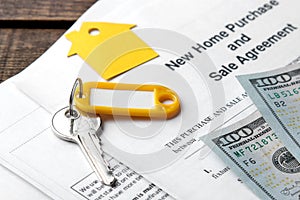 New home purchase and sale agreement. Key with keyring and blank and money on a brown wooden table. concept of buying a home