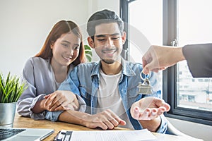 New house / home moving and relocation concept. Happy asian couple receiving apartment key from real estate agent / realtor