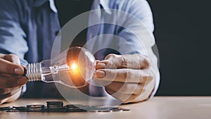 New idea concept with coins stack save power to save the earth, young Asian men hand holding light bulb  with new knowledge light