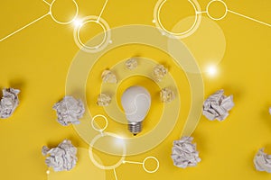 New idea concept with crumpled office paper and white light bulb on yellow background. Creative solution during brainstorming photo