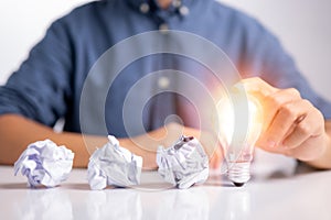 New idea and light bulb concept with man hand touching light bulb and three crumpled office paper. Businessman show new ideas