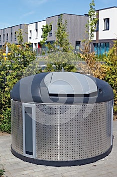 A new large modern stainless steel trash bin is installed on a city street