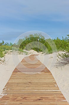 New light brown planks boardwalk in white sand dunes.