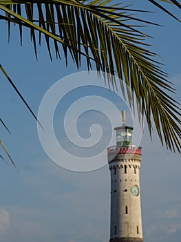 New Lindauer Lighthouse against the blue sky with palm tree leaves in the foreground in Germany