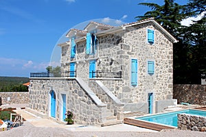 New Mediterranean villa built with stone in traditional style with blue wooden window blinds and doors next to swimming pool