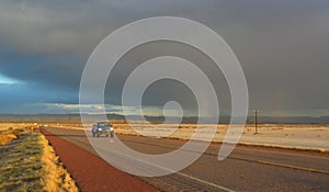 NEW MEXICO, USA - NOVEMBER 22, 2019: rainbow and car on the road during a red sunset and thunderclouds on the background of the