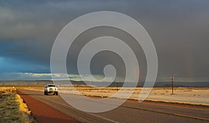 NEW MEXICO, USA - NOVEMBER 22, 2019: rainbow and car on the road during a red sunset and thunderclouds on the background of the