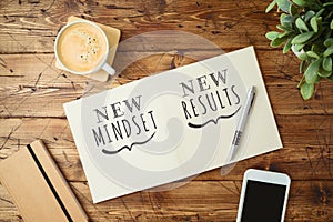 New mindset and new results text on notebook on wooden table with coffee cup and smartphone Business concept of positive thinking