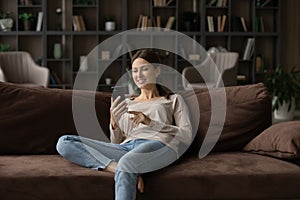 Young woman spend leisure holds smartphone while relaxing at home