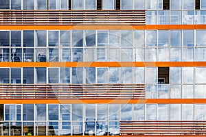 A new modern building of student dormitorie in the campus with many windows with reflections of blue sky with white clouds.