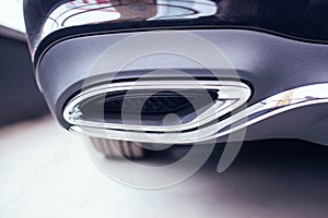 New modern chrome tailpipe on a black passenger car. Tuned muffler and beautiful bumper, transportation photo