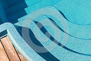 New modern fiberglass plastic swimming pool entrance step with clean fresh refreshing blue water on bright hot summer