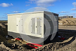 New modern grey electric transformer room building with yellow hazard signs on blue sky background