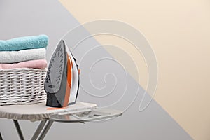 New modern iron and basket with laundry on board against color background, space for