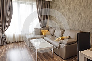 New modern living room. New home. Interior photography. Wooden floor. Sofa near the windows with long curtains