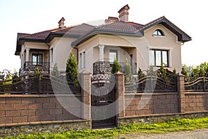 New modern luxurious expensive residential two story cottage house with shingle roof, big windows and balconies behind stone fence