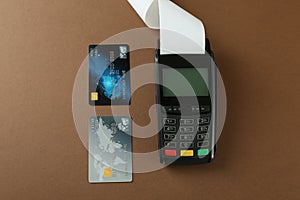 New modern payment terminal and credit cards on brown background, flat lay