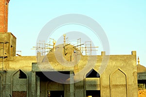 A new mosque under construction against the sunny blue sky with the mosque minaret and the domes surrounded with wood scaffold