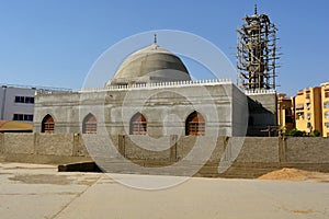 A new mosque under construction against the sunny blue sky with the mosque minaret surrounded with wood scaffold