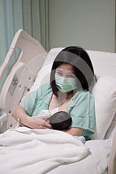 New mother with mask feeding newborn baby on bed at hospital