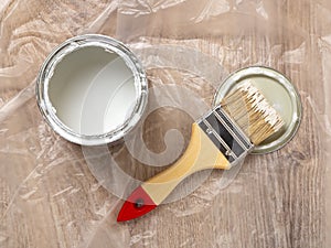 New natural bristle brush with paint on a lid near an open paint can over cellophane covered floor. Construction painting work,