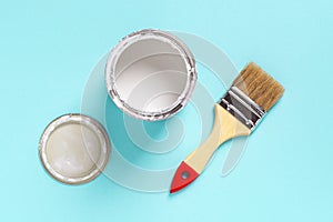 New natural bristle brush with wooden handle, open white paint can and lid on a cyan blue background. Construction painting work,