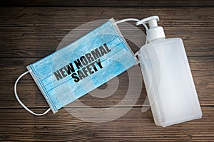 NEW NORMAL SAFETY text with safety face mask and hand sanitizer on wooden background