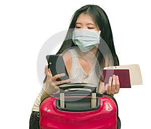 New normal traveling - young happy and beautiful Asian Korean woman in face mask carrying suitcase holding passport using mobile