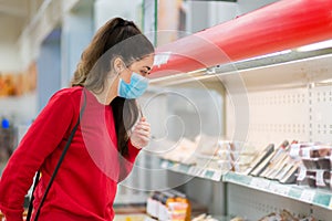 The new normal. A young woman in a protective mask selects products in a supermarket window. Side view. The concept of shopping