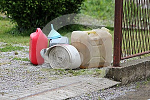 New and old plastic fuel canisters with plastic funnel next to used wide fire hose prepared for using with water pump to prevent