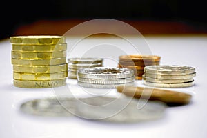 The new one pound as vertical and stack of British currency coins on white table and black ground