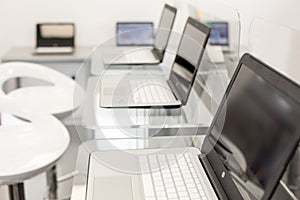 New, open laptops, on a glass desktop; modern white chairs in background