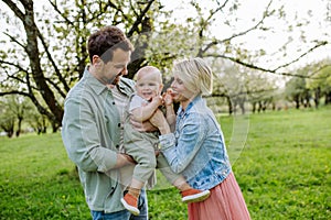 New parents holding small toddler, baby, outdoors in spring nature. Older First-time parents.