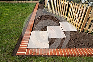 New paving stones  installed in front of a picket fence protecting a garden pond,  within a flower bed area