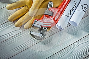 New plumb wrench leather gloves and rolled piping blueprints on vintage wood background