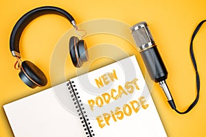 NEW PODCAST EPISODE text on notepad next to headphones and recording microphone