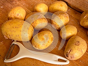 New potatoes and white peeler on a wooden worktop