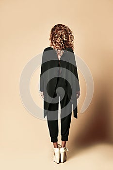 New pretty modern style dancer curly hair woman walking posing in designer black cloth full body on beige background