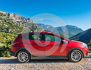 A new red car pulled over on the side of a remote mountain road