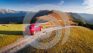 A new red car pulled over on the side of a remote mountain road